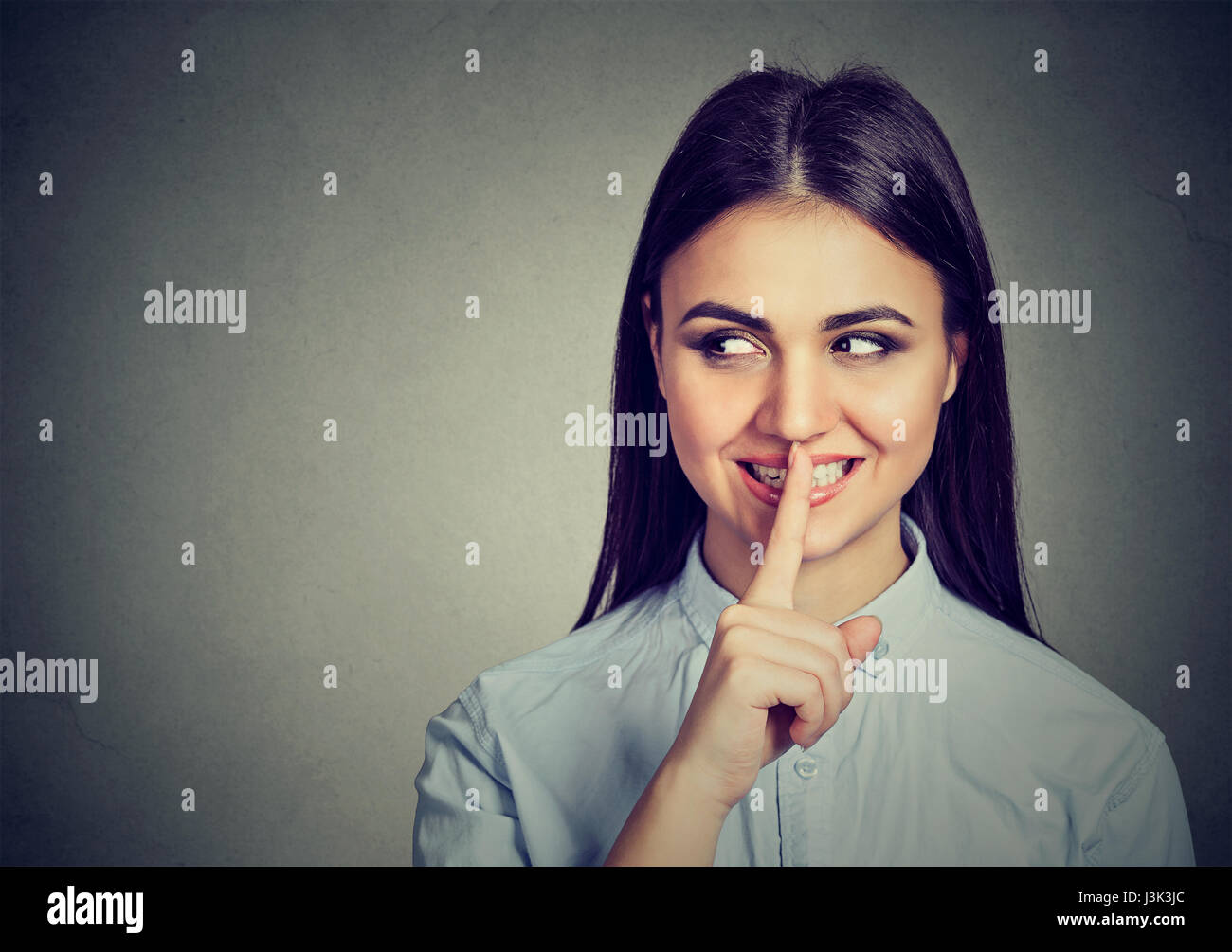 Happy secret girl. Woman saying hush be quiet with finger on lips gesture isolated on gray wall background. Stock Photo