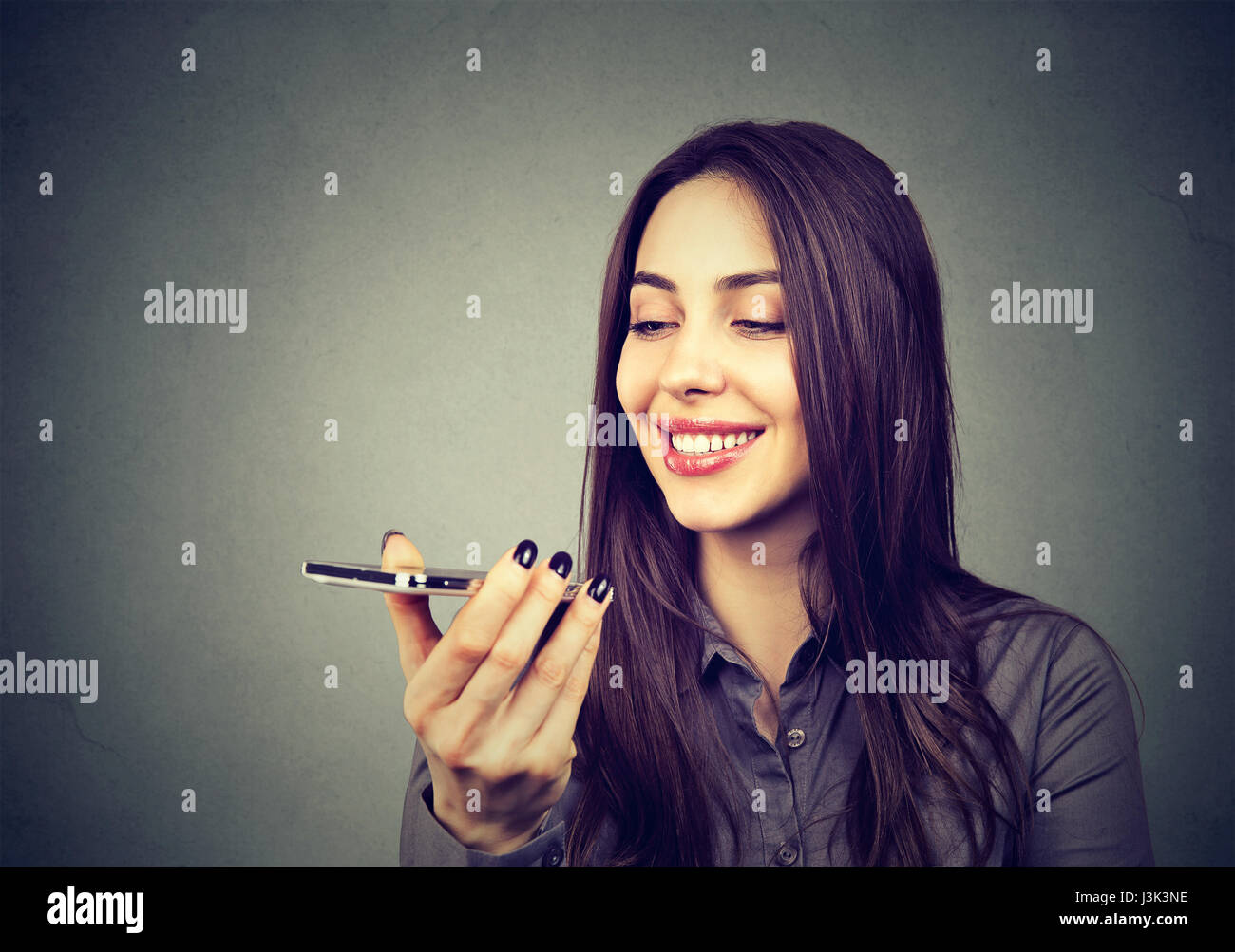 Girl using a smart phone voice recognition function on line on gray wall background Stock Photo