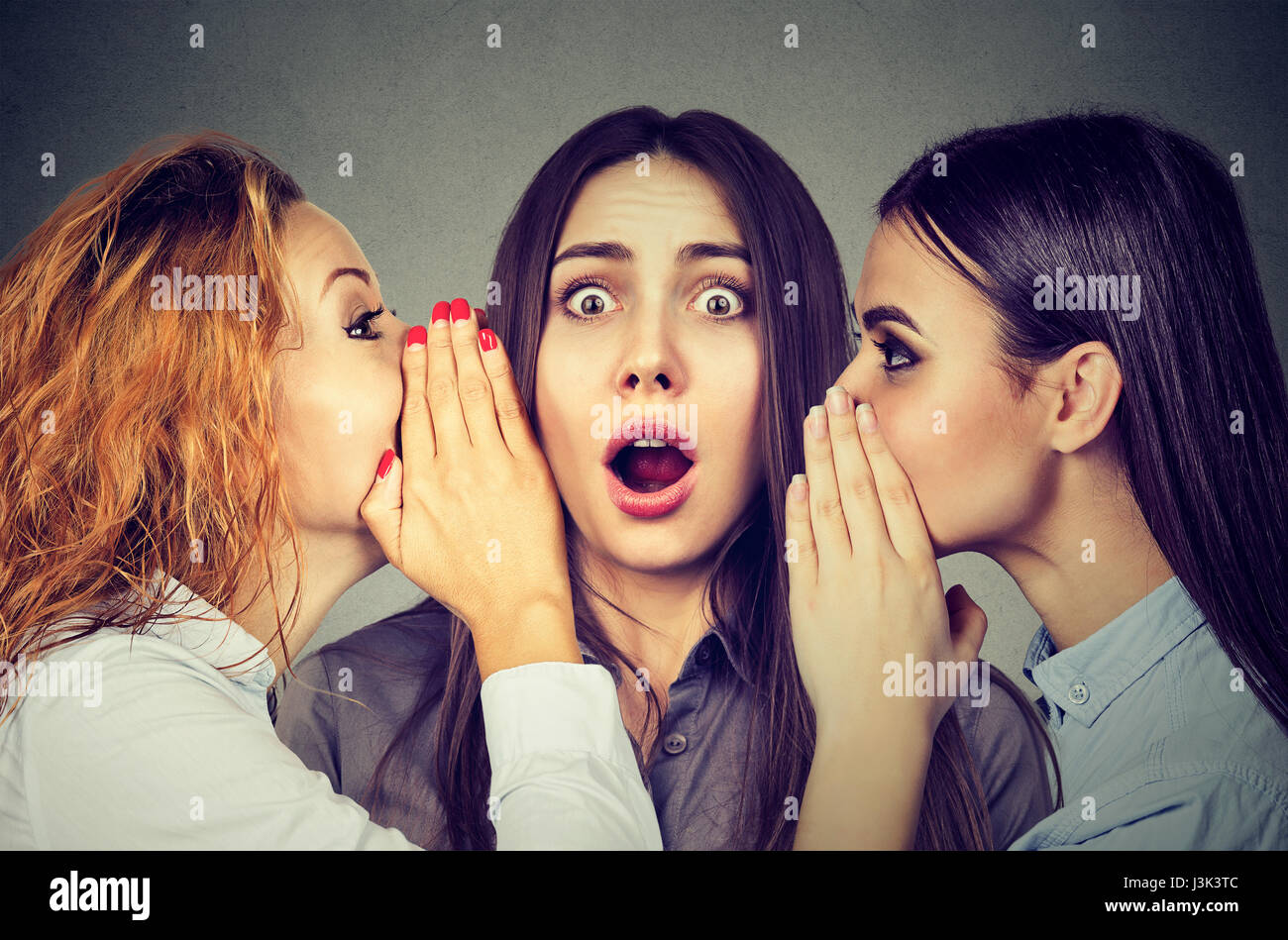 Three young women telling whispering a secret gossip each other in the ear Stock Photo