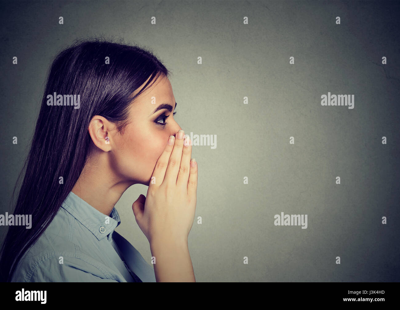 Closeup portrait of a woman whispering a gossip isolated on gray wall background Stock Photo
