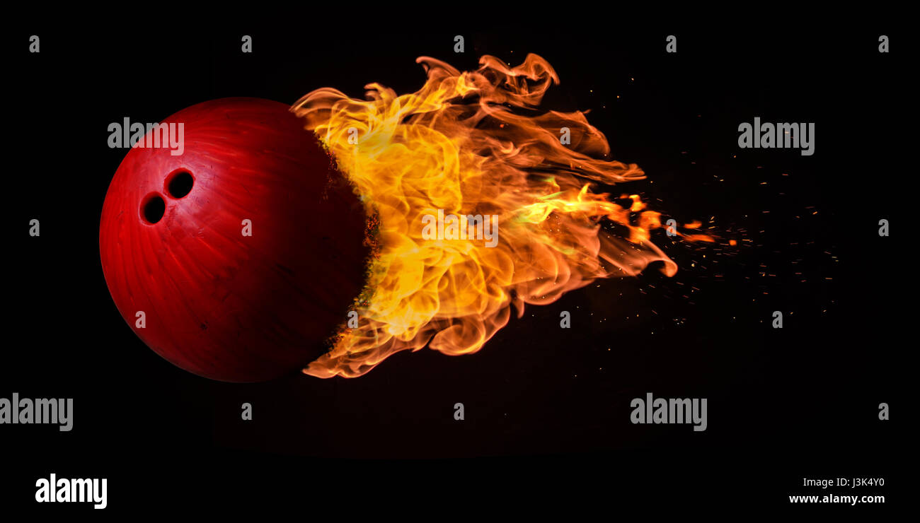 Flying bowling ball engulfed in trailing flames with sparks flying on a black background. Concept of a fiery competition or fast moving ball. Stock Photo