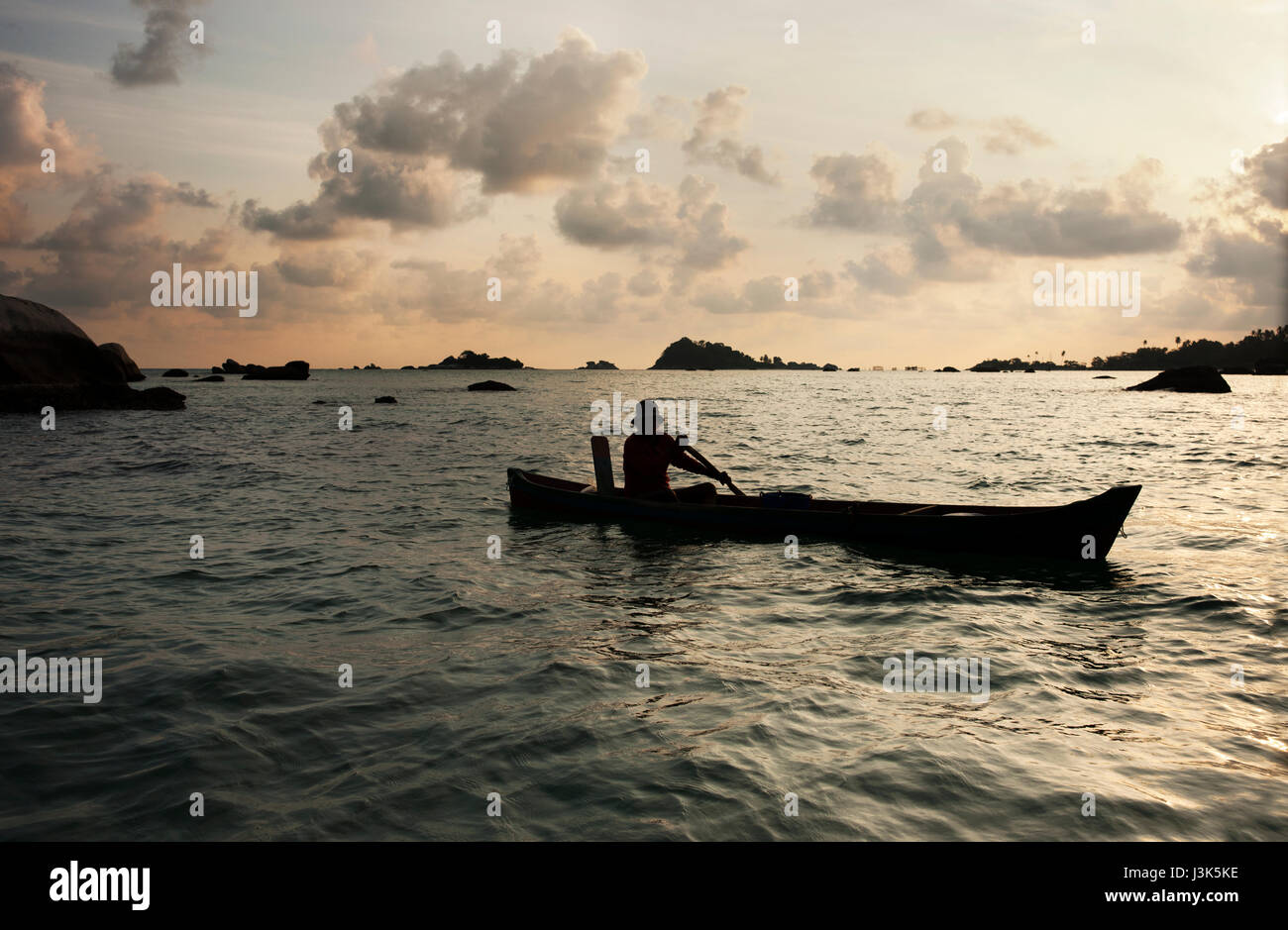 Silhouette of one man rowing a small boat with his paddle on the ocean at sunset, Belitung Indonesia. Stock Photo