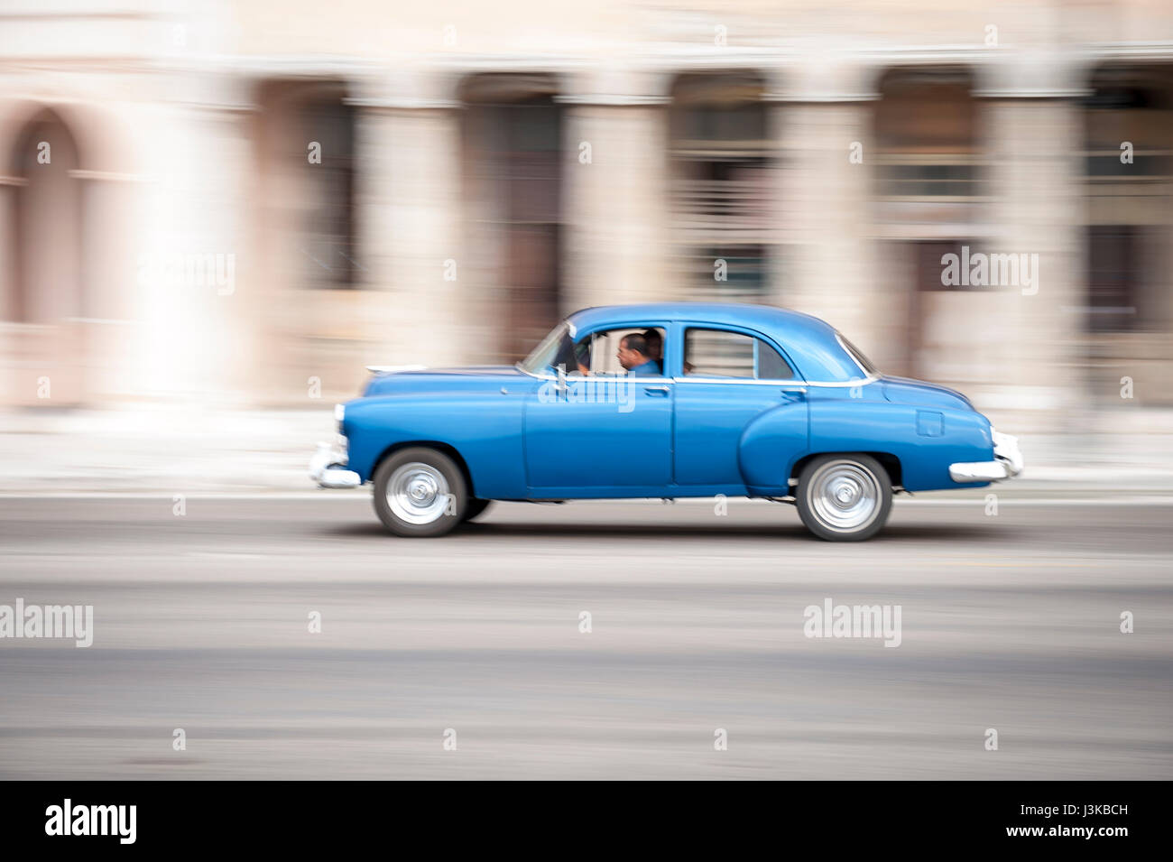 Classic blue American car serving as taxi drives in front of classic colonial architecture on the Malecon in Central Havana, Cuba Stock Photo