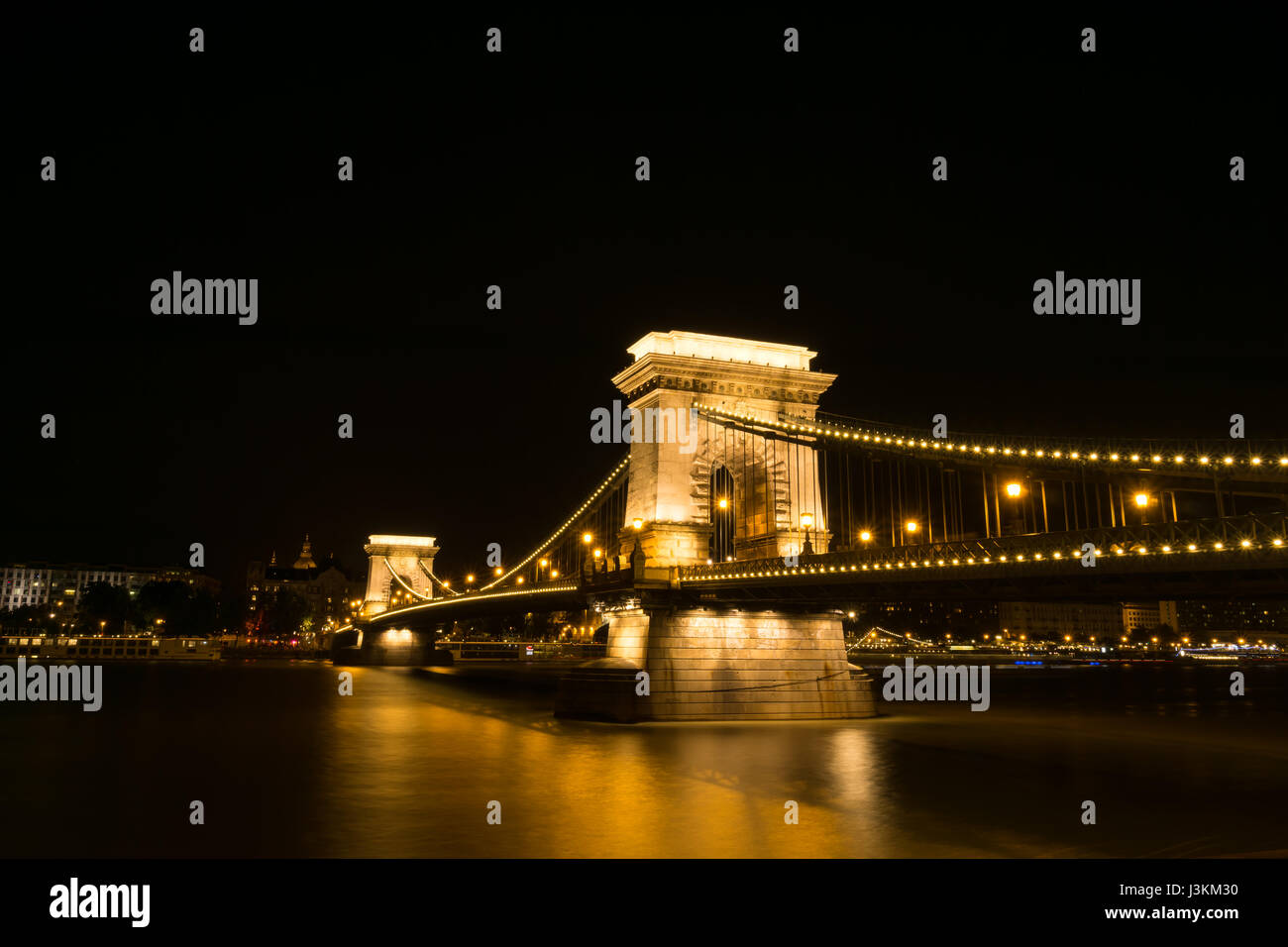 Golden lights illuminate Budapest's historic Chain Bridge which spans the River Danube, view from Buda to Pest. Stock Photo