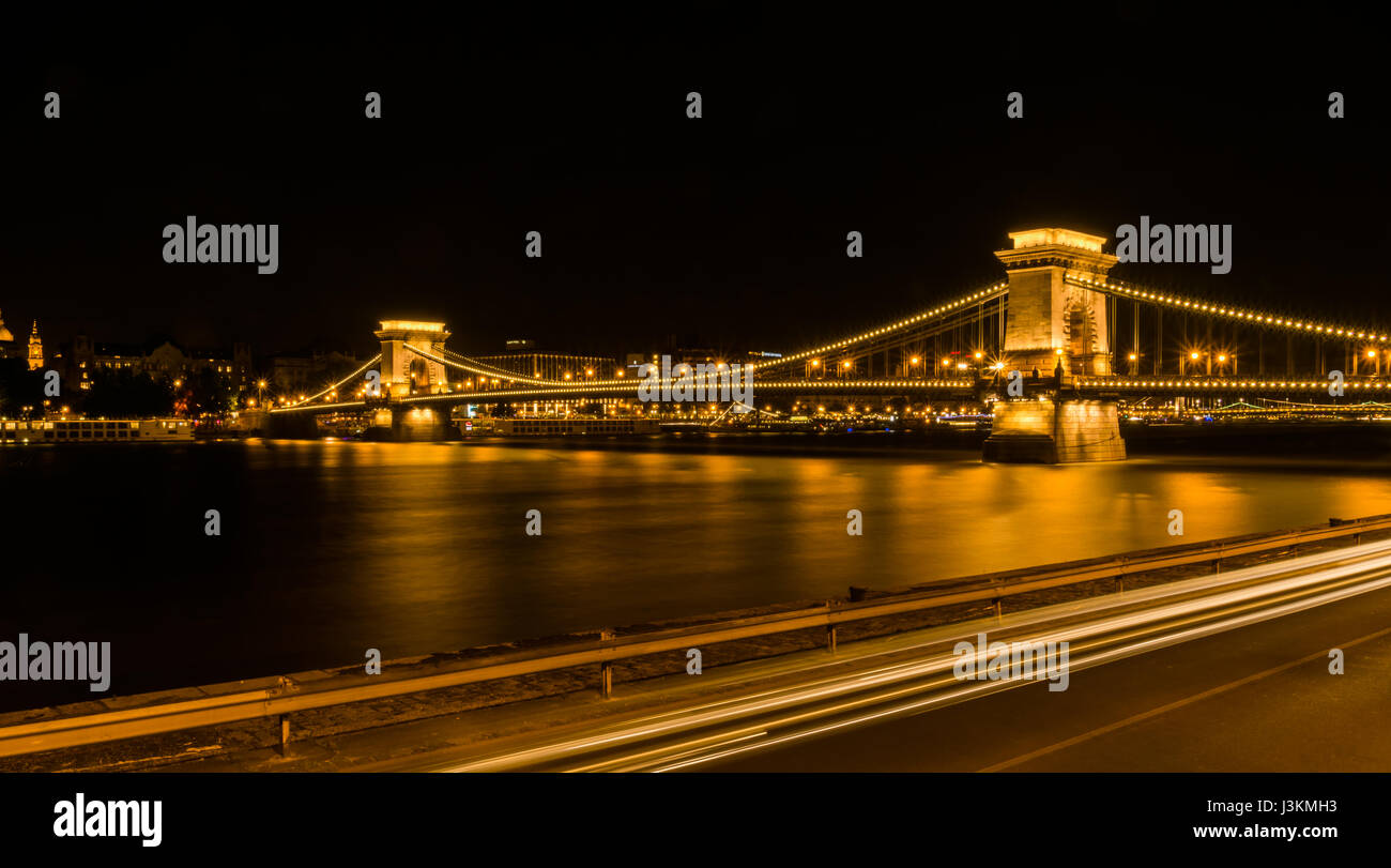 Night time view of the iconic Chain Bridge that spans the River Danube, with the bridge and city skyline of Budapest lit up in golden lights. Stock Photo