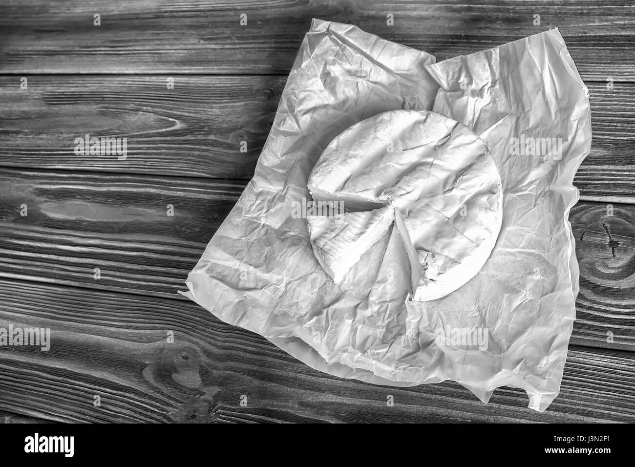 Camembert cheese on white paper and rustic dark wooden background. Top view. Black and white Stock Photo