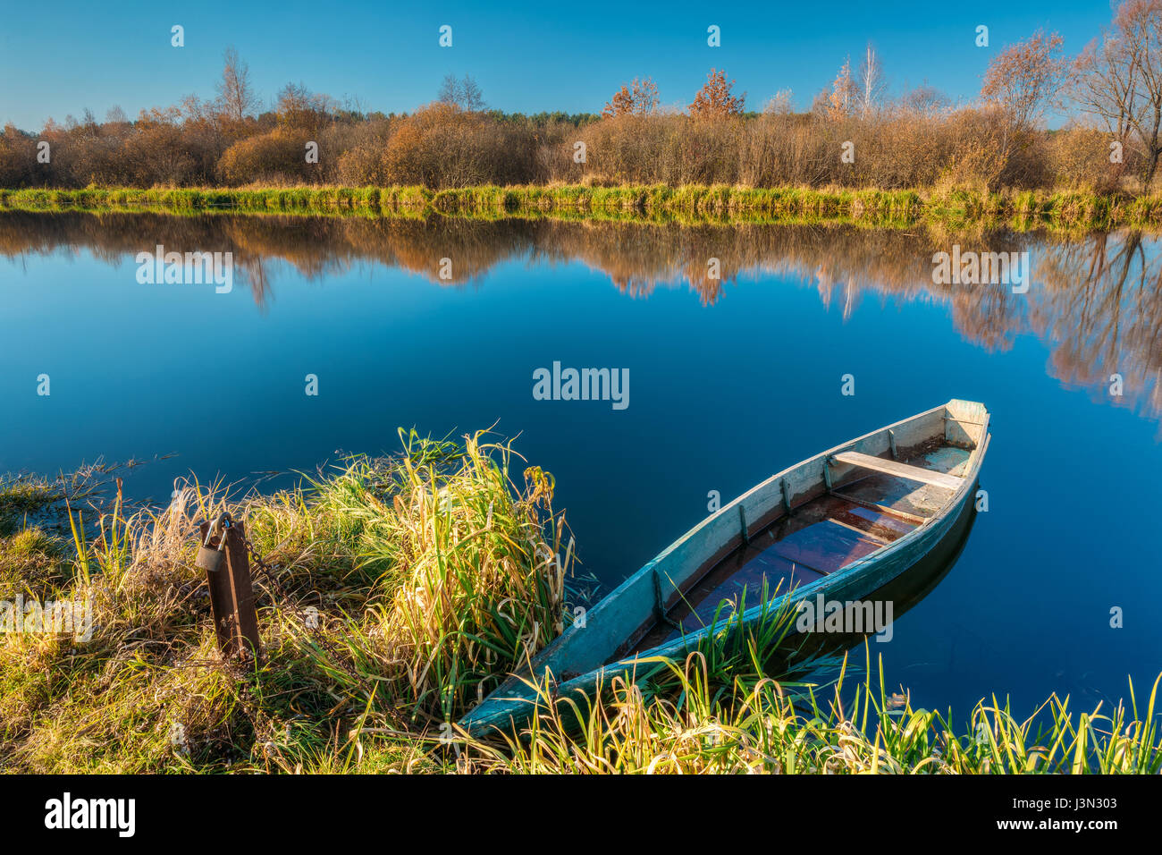The Picturesque Autumn Fall River Landscape, Yellowed Bank Of River With One Tied Up Wooden Small Blue Fishing Rowboat Skippet On The Motionless Water Stock Photo