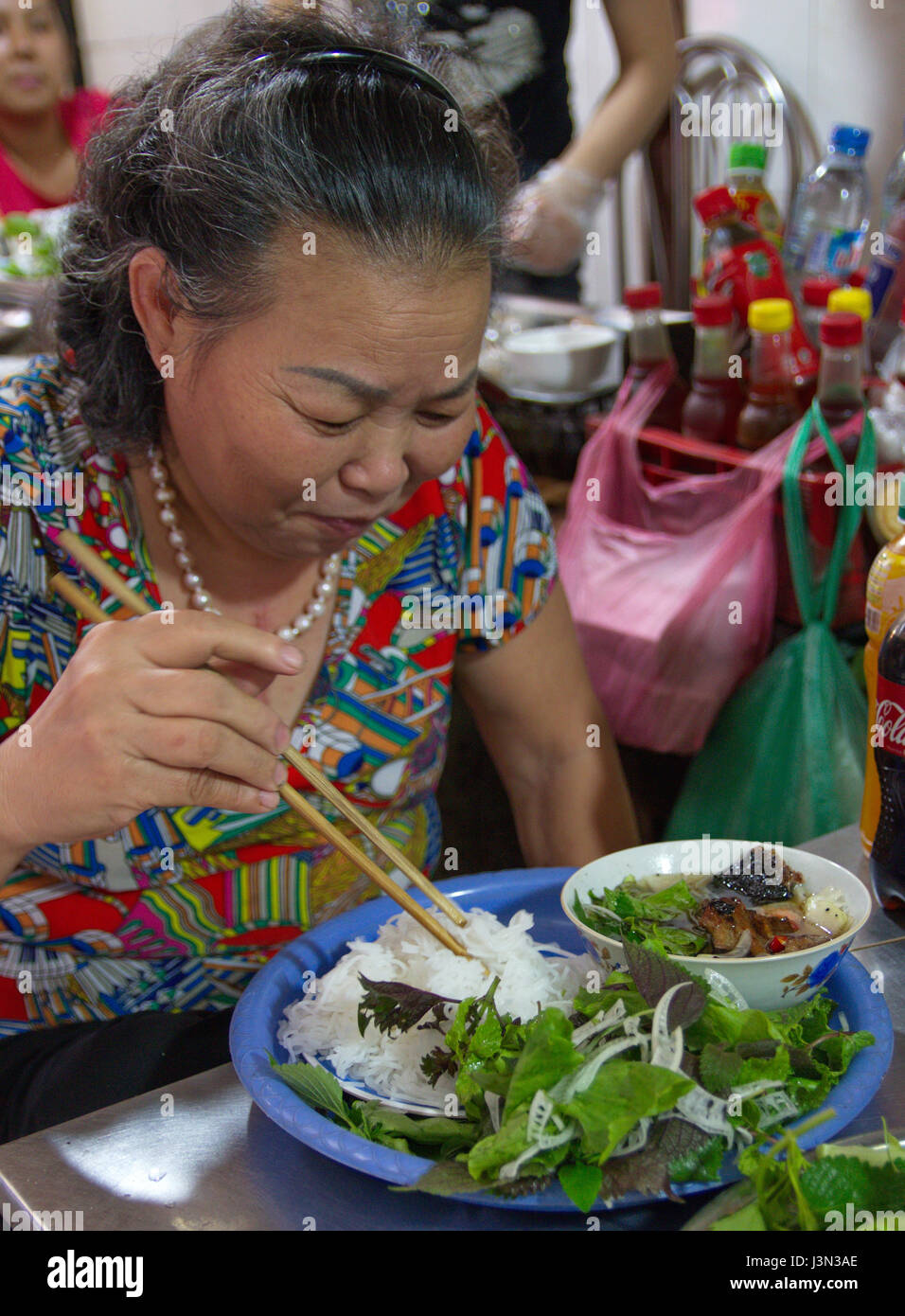 Vietnamese woman eating noodles at a street stall in Hanoi, Vietnam Stock Photo