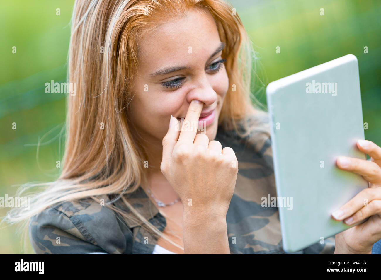 funny portrait of a girl picking her nose while reading on a digital tablet something she found out in the internet Stock Photo