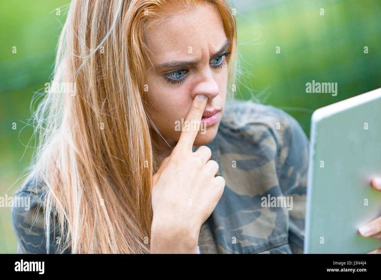 funny portrait of a girl picking her nose while reading on a digital tablet something she found out in the internet Stock Photo