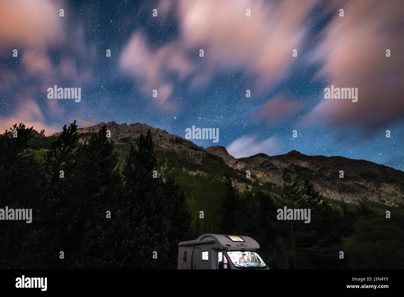 Camper van under moonlight, starry sky and blurred motion clouds on the ...