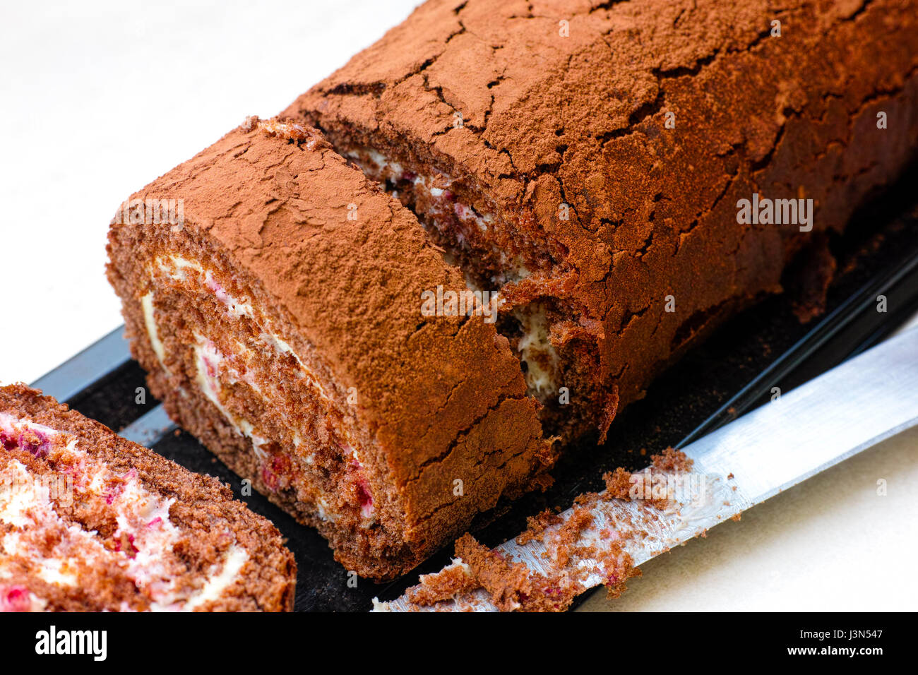 Slices of tasty chocolate sponge cake roll with cream and knife. Stock Photo