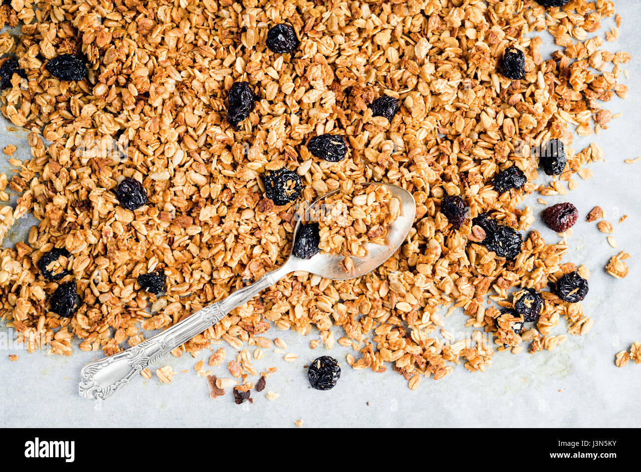 Homemade oat, cherry and coconut granola over baking paper with spoon,  Stock Photo