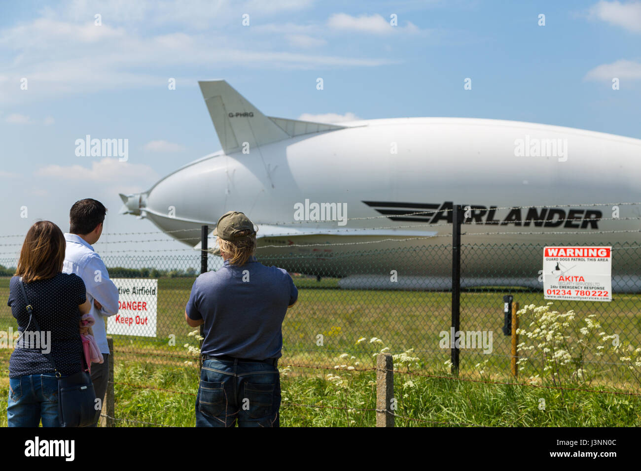 Cardington, Bedfordshire, UK. 7th May, 2017. The Hybrid Air Vehicles Airlander 10 on the new Mobile Mooring Mast at Cardington Airfield. Spectators enjoy the view whilst security sensors on posts inside the fence keep out unwelcome intruders as the aircraft, HAV 304 is almost ready to begin it's 2017 flight test programme. Photo Credit: Mick Flynn/Alamy Live News Stock Photo