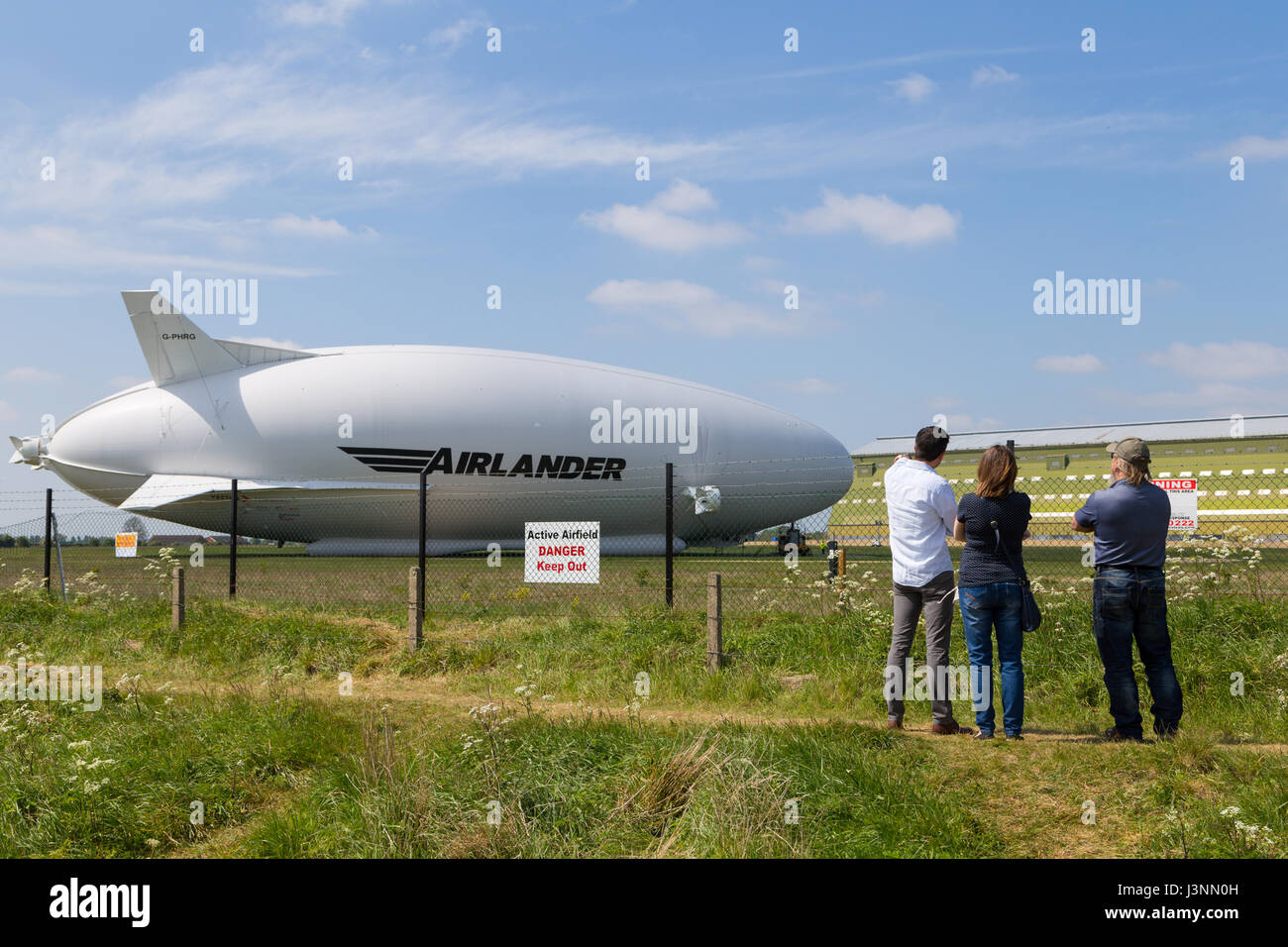 Cardington, Bedfordshire, UK. 7th May, 2017. The Hybrid Air Vehicles Airlander 10 on the new Mobile Mooring Mast at Cardington Airfield. Spectators enjoy the view whilst security sensors on posts inside the fence keep out unwelcome intruders as the aircraft, HAV 304 is almost ready to begin it's 2017 flight test programme. Photo Credit: Mick Flynn/Alamy Live News Stock Photo