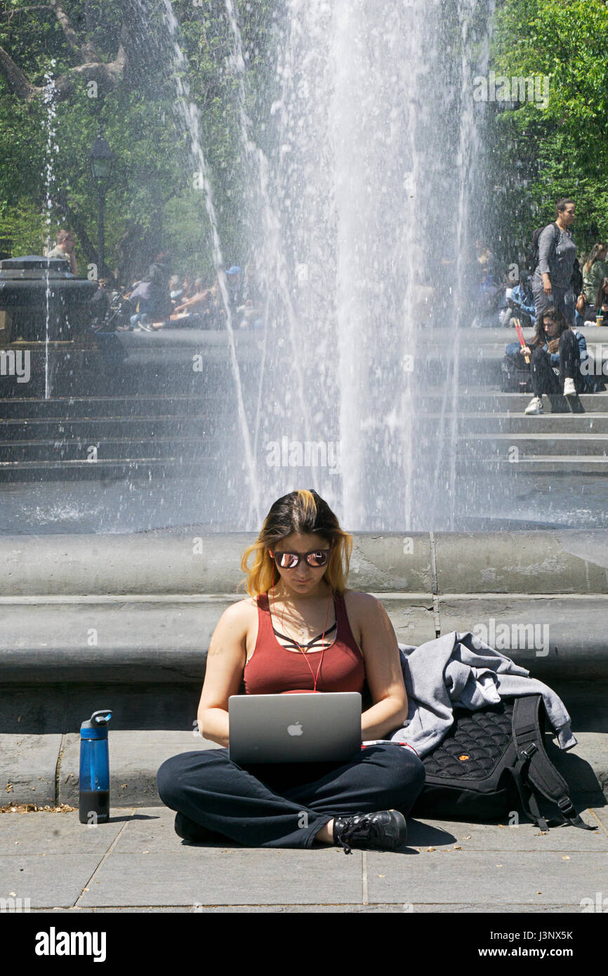 Portrait of a young lady working on her computer outdoors in Washington Square Park without being distracted by other people. Stock Photo