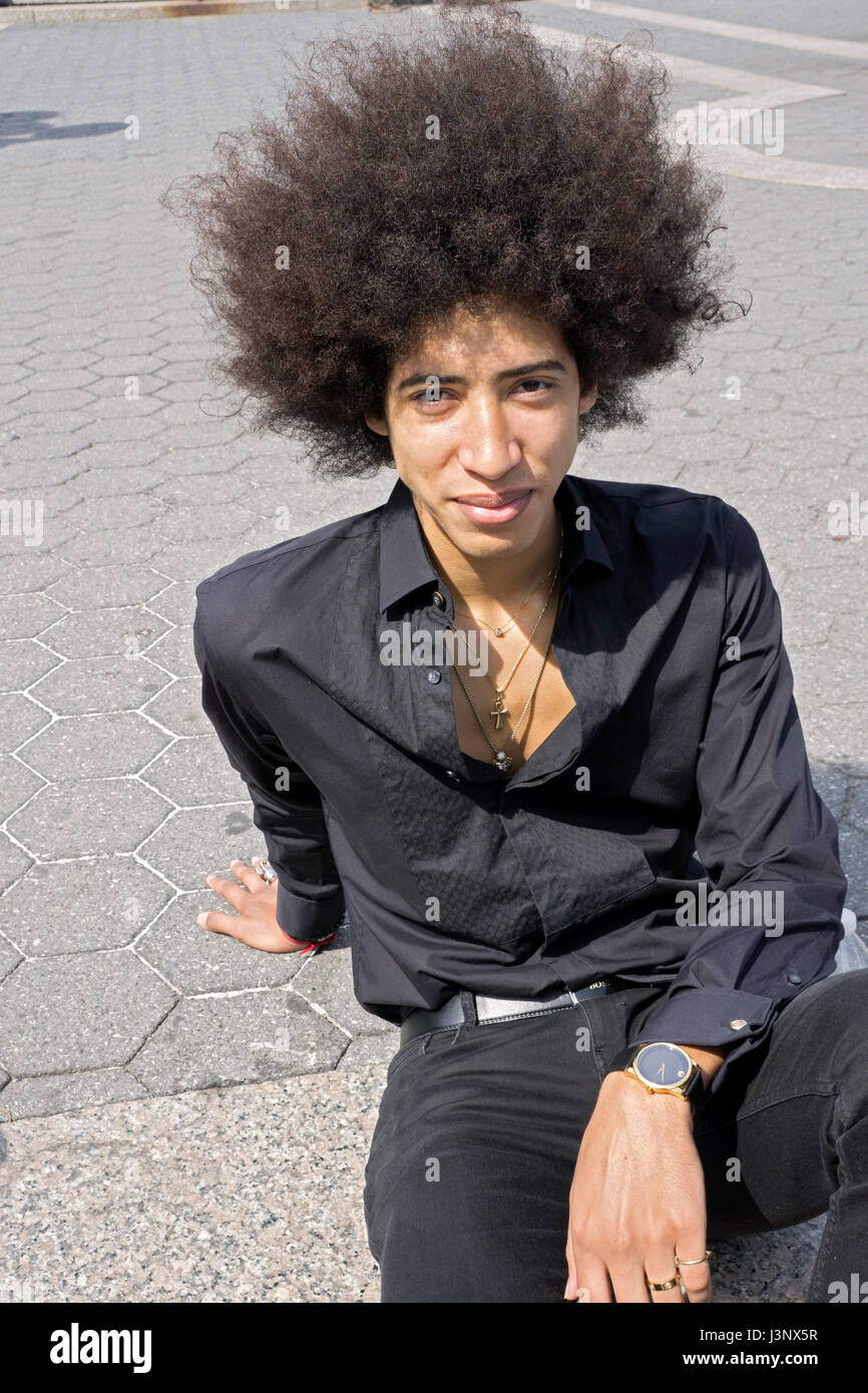 A twenty year old man dressed in all black with a large Afro hairdo. In Nuion Square Park in Manhattan, New York City. Stock Photo