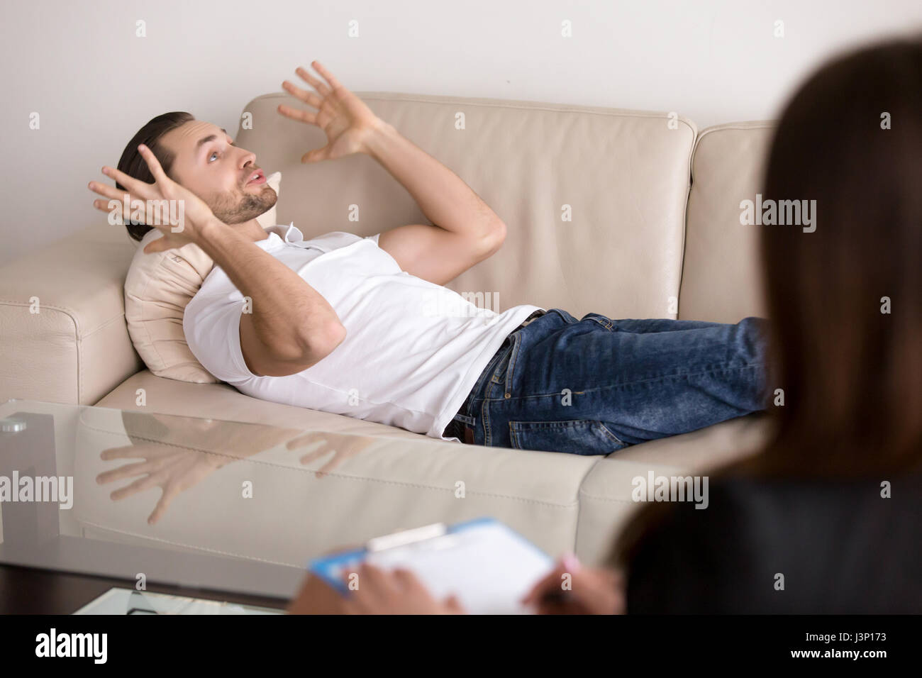 Young male patient lying on couch talking to female psychologist Stock Photo