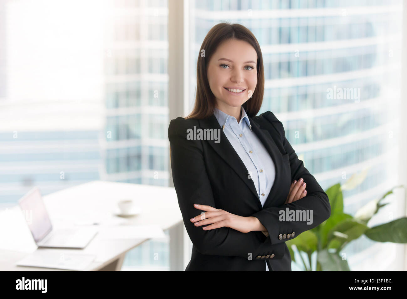 Young confident smiling businesswoman standing in office with ar Stock ...