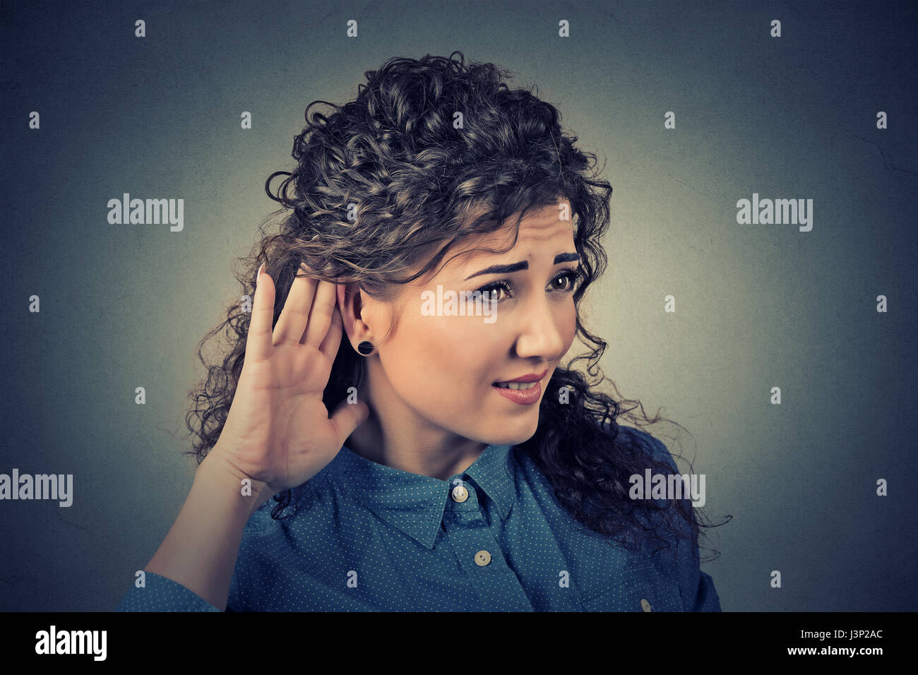 Closeup portrait young nosy woman hand to ear gesture carefully intently secretly listen in on juicy gossip conversation news isolated on gray backgro Stock Photo