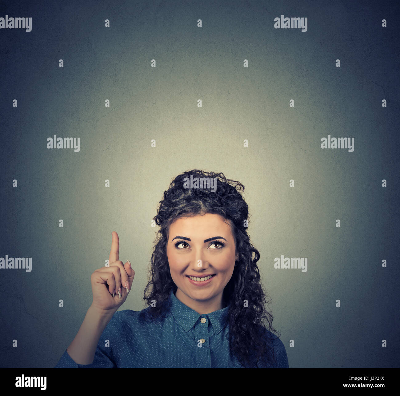 Portrait happy beautiful woman thinking looking up pointing finger at blank copy space above head isolated on grey wall background. Positive human fac Stock Photo