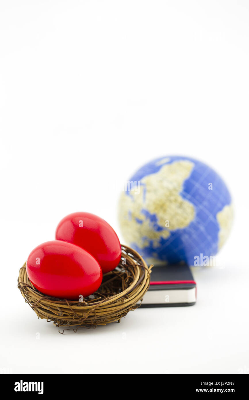 Vertical image with focus on two, red nest eggs with journal and globe behind. Conceptual image of global market and investing risks. Stock Photo