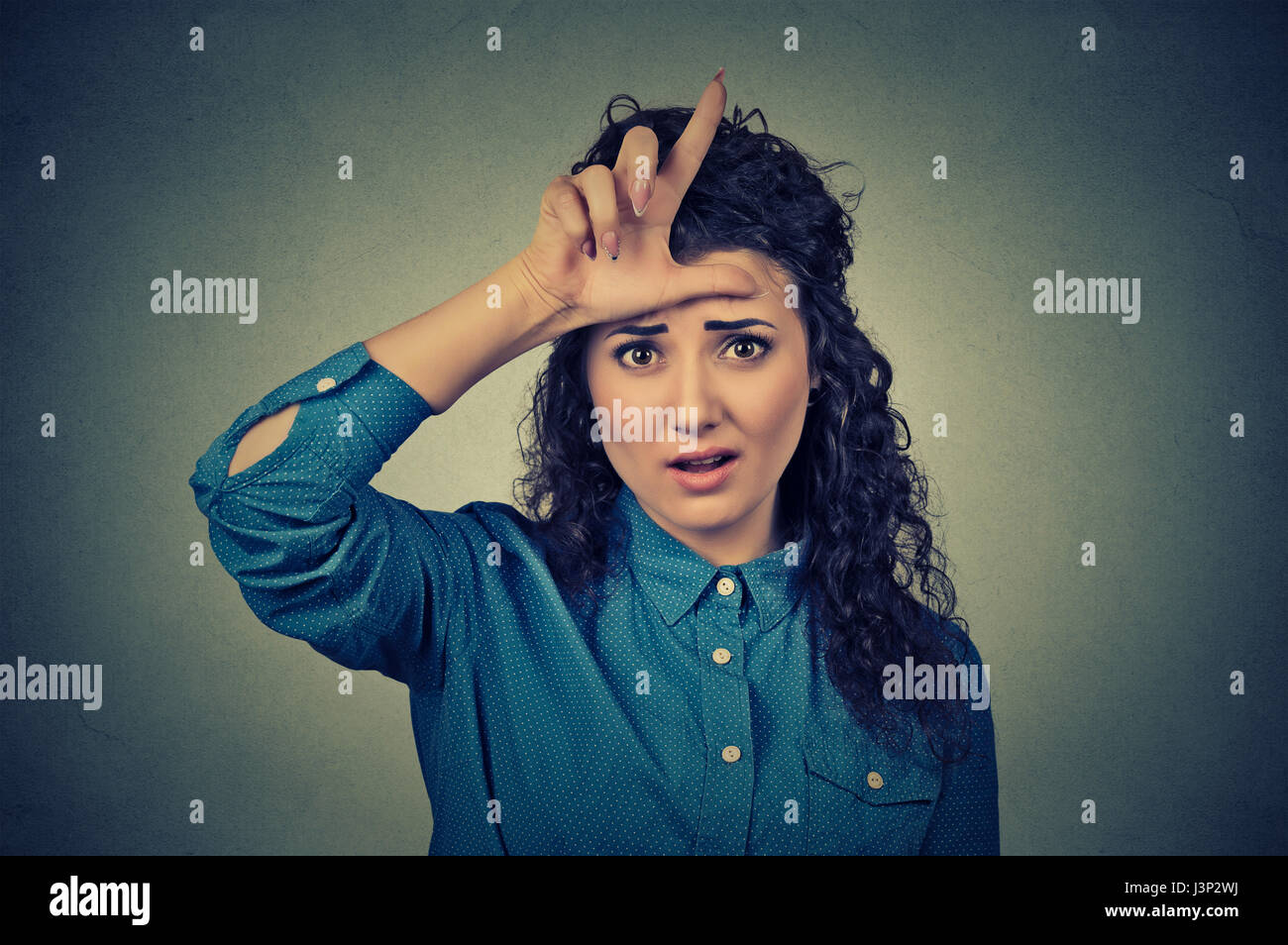Closeup portrait young unhappy woman giving loser sign on forehead, looking at you, disgust on face isolated on gray wall background. Negative human e Stock Photo