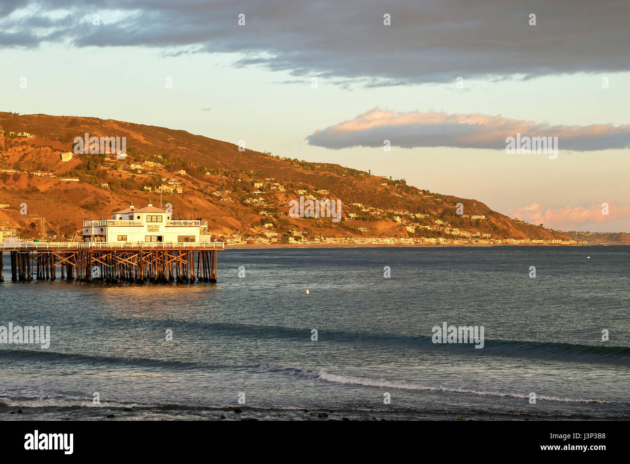 Sun is about to set at Malibu Pier casting warm lights to the hills, Malibu California Stock Photo