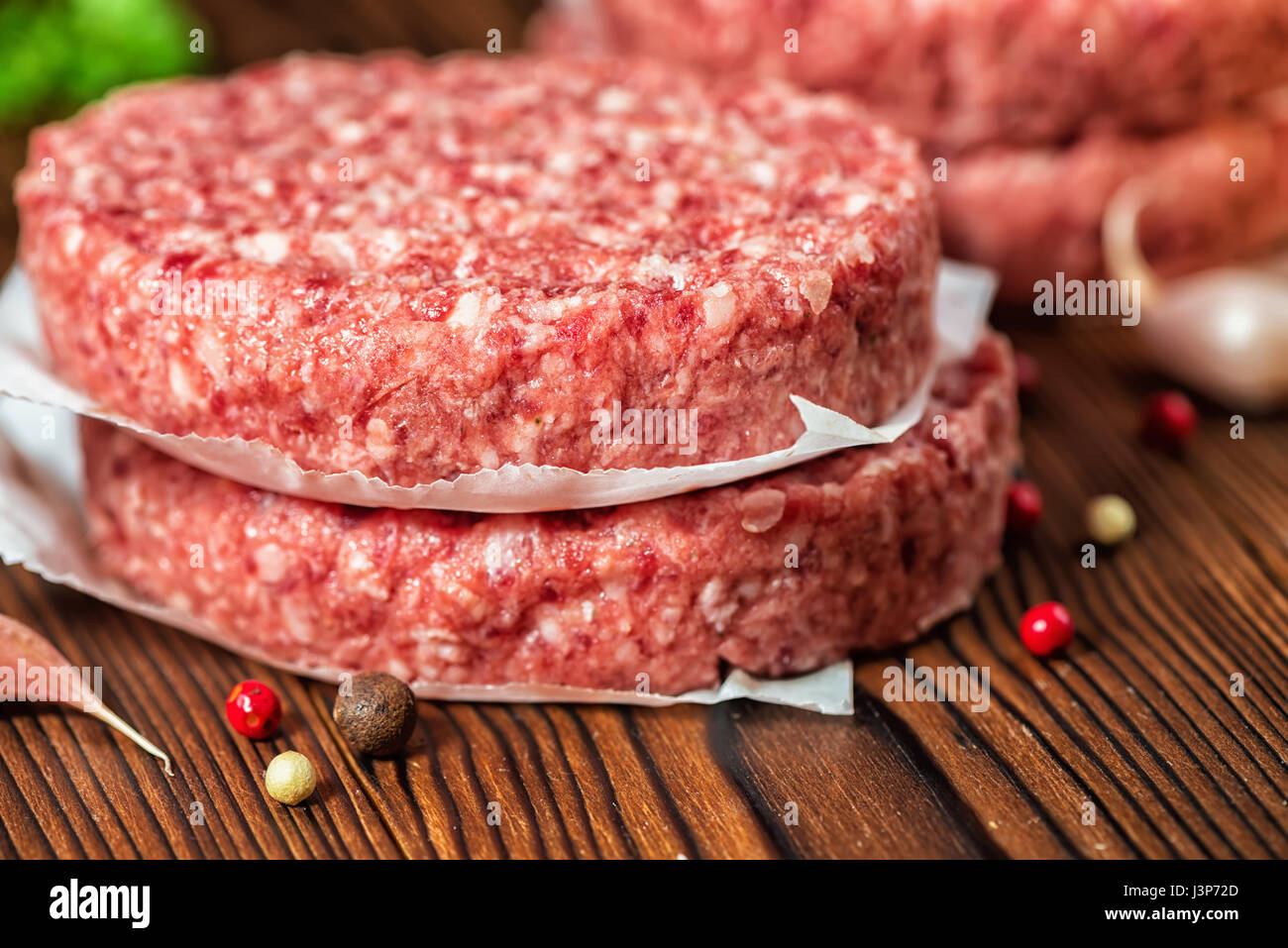 raw ground beef meat hamburger patties on paper, dry pepper and garlic on wooden background