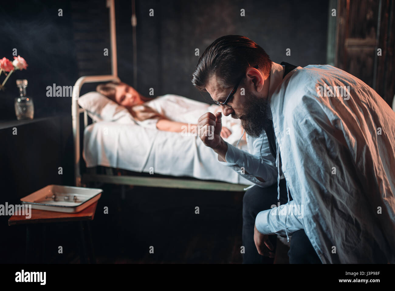 Tired man sitting against young sick woman in the hospital bed. Illness of female patient in clinic, health recovery and treatment Stock Photo