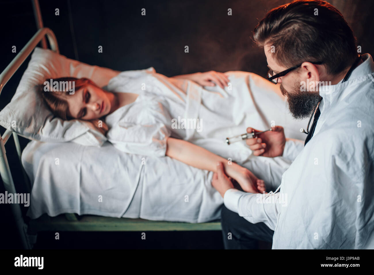 Male doctor makes syringe injection to sick woman in hospital bed. Sickness of female patient in clinic, health recovery and treatment Stock Photo