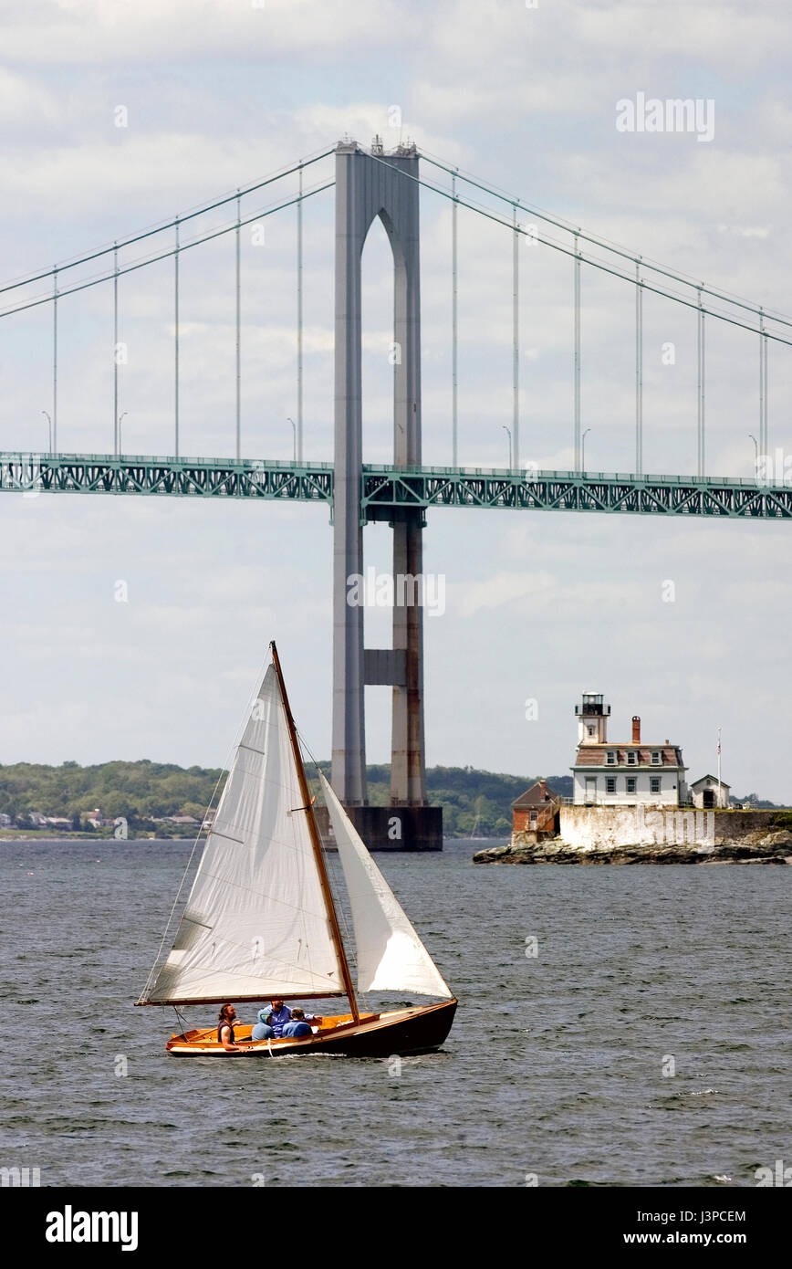A sailboat passes the Clayborn Pell (Jamestown) Bridge and Rose Island Light off Newport, RI Stock Photo