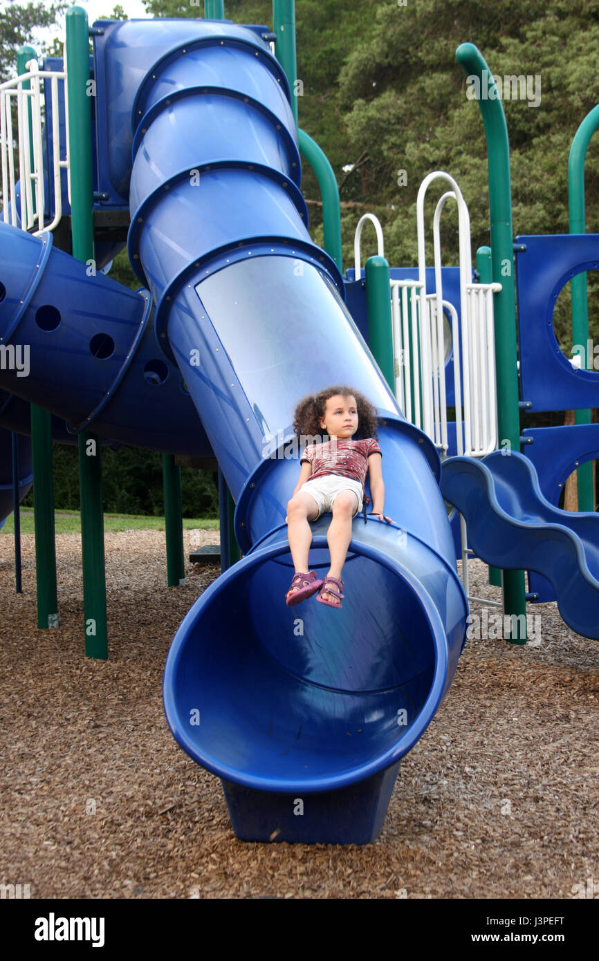 Little girl sitting on blue slide at playground Stock Photo