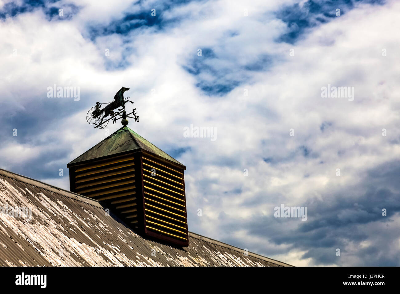 Wweather vane on roof of house against the clouds Stock Photo