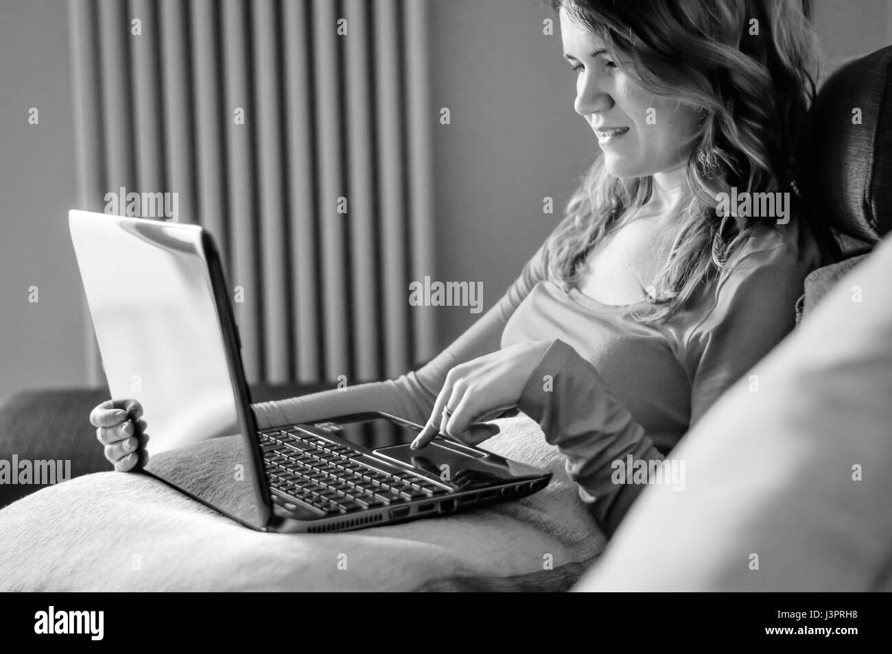 Young woman working from home on laptop on the couch, black and white image Stock Photo