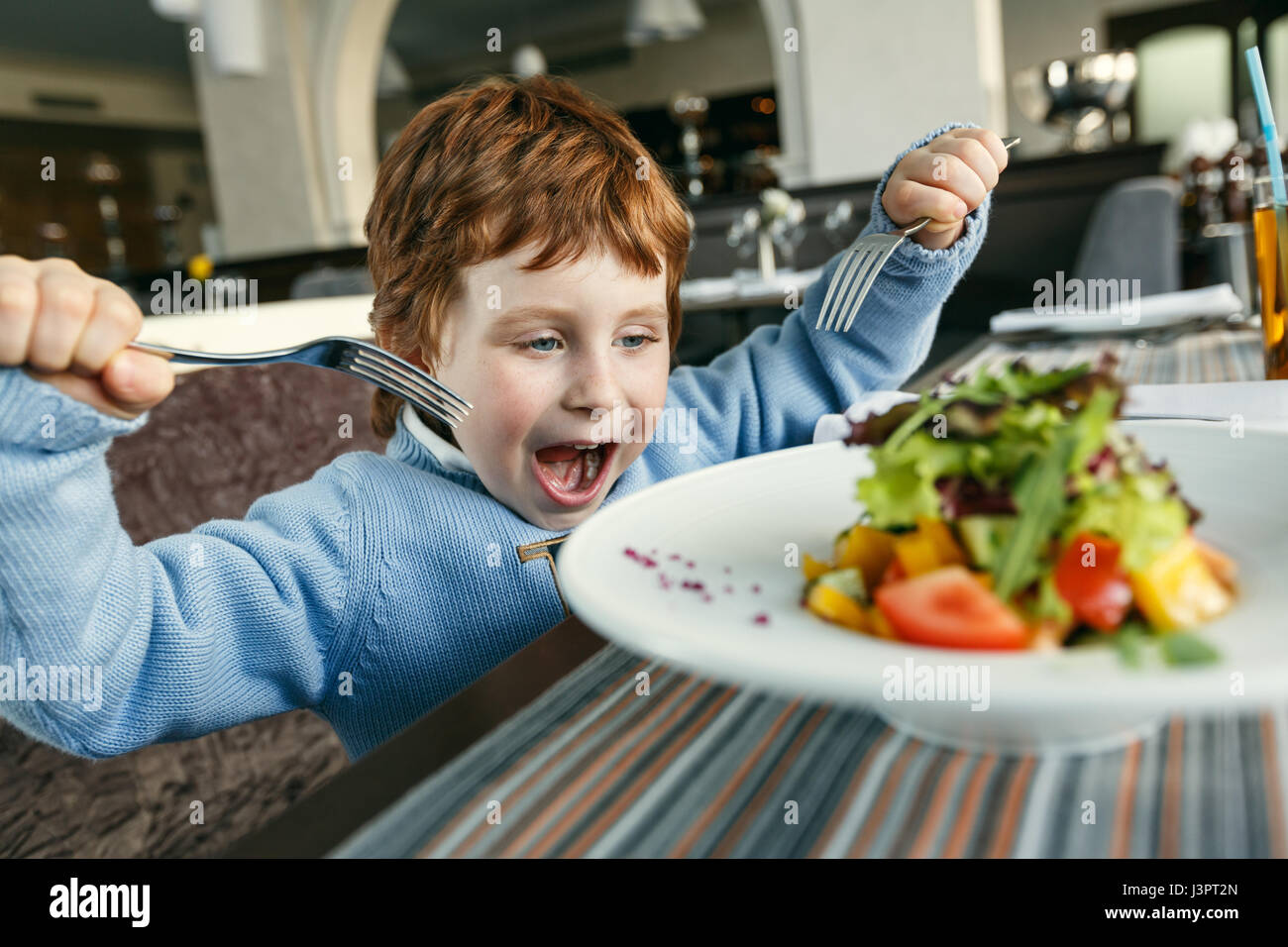 Little red haired boy with two forks eating salad in a restaurant Stock  Photo - Alamy