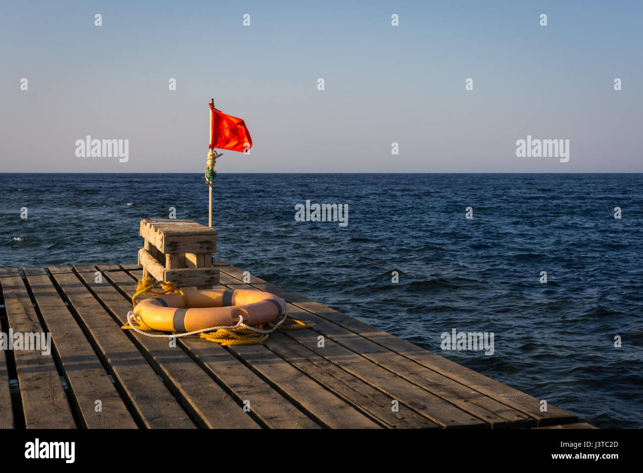 Red flag for warning and lifebelt on a  old wooden pier for diving and snorkeling at sunset.copy space. Stock Photo