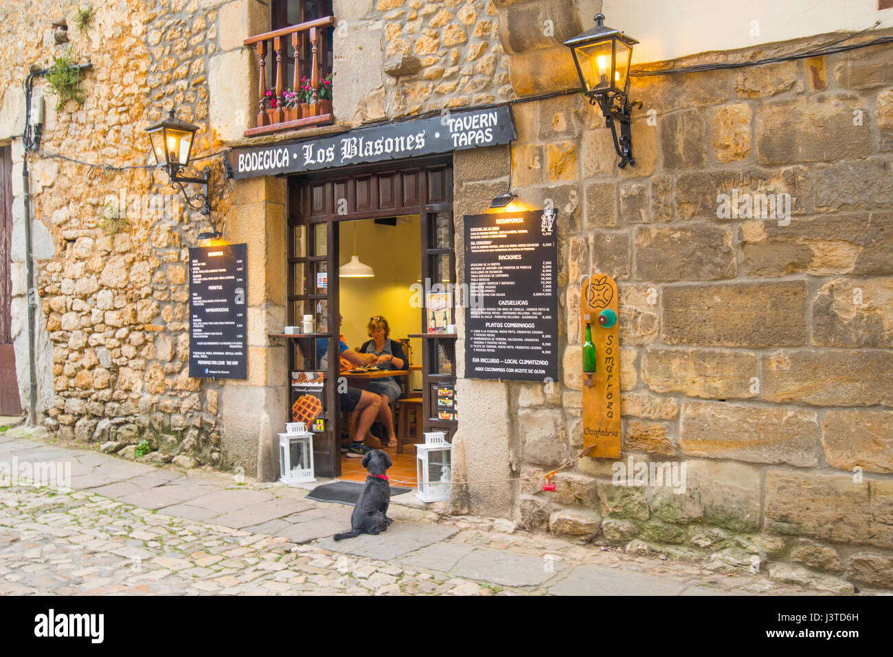 People having tapas in a typical tavern and dog waiting for them by the door. Santillana del Mar, Cantabria, Spain. Stock Photo