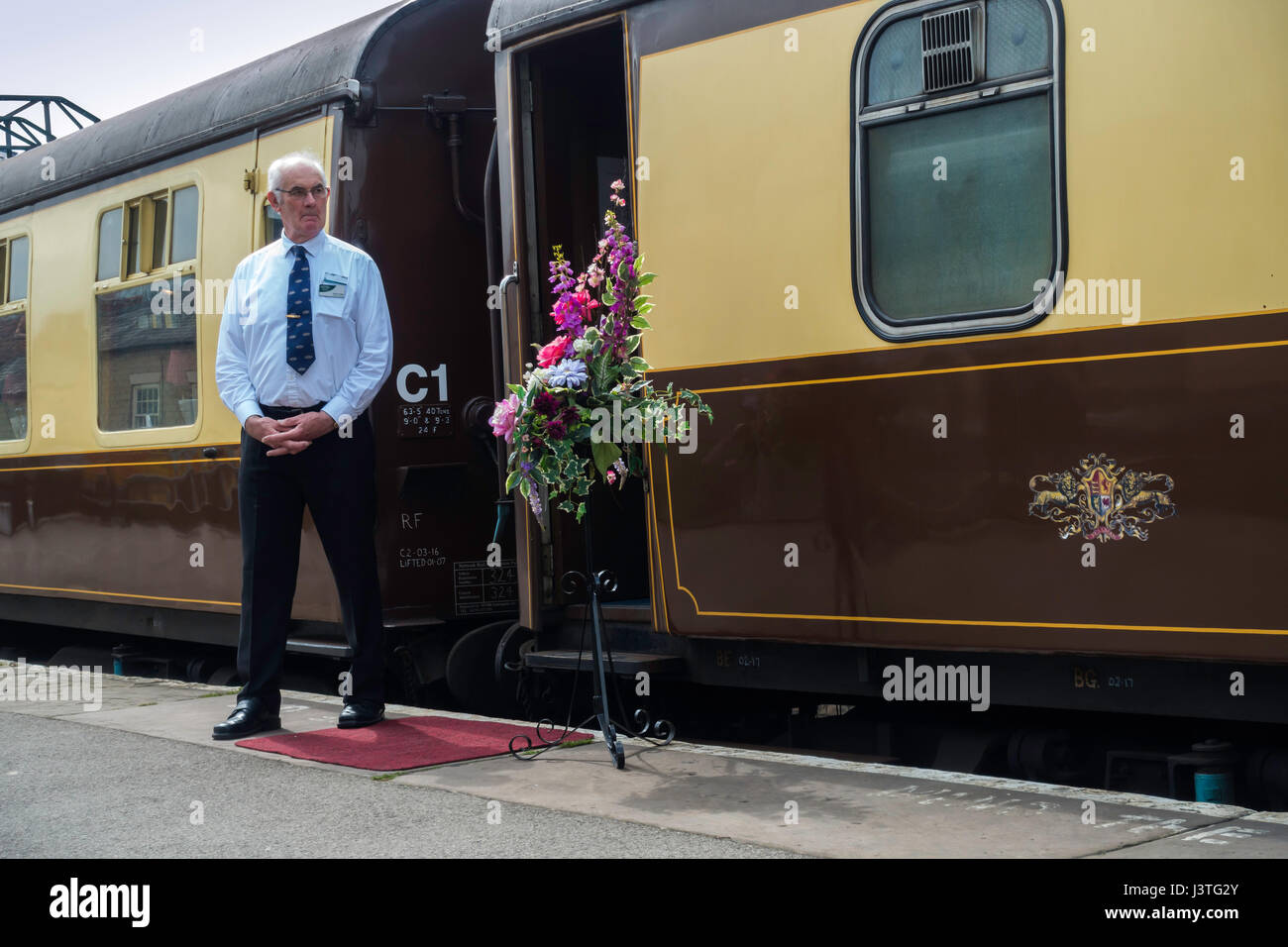 Pullman Manager waiting to welcome passengers on board a Whitby train at Pickering on the North Yorkshire Moors Railway April 2017 Stock Photo