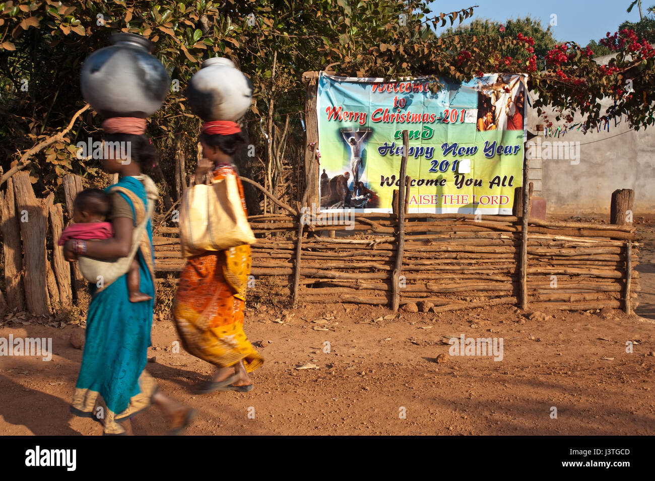 Two tribal women are walking in front of a poster celebrating christian festivities ( India) Stock Photo