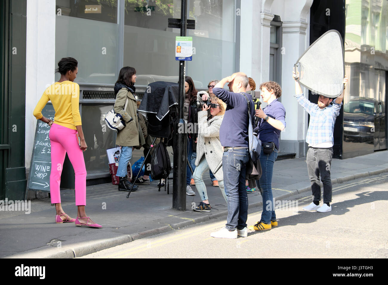 Film crew female photographer photographing young black fashion model in pink trousers and yellow top in Beak Street, Soho, London W1 UK  KATHY DEWITT Stock Photo