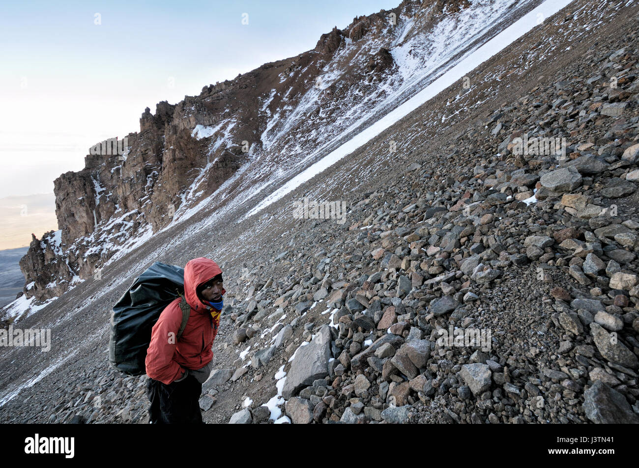 A porter carrying a big backpack climbing the Western Breach, Mount Kilimanjaro National Park, Tanzania Stock Photo