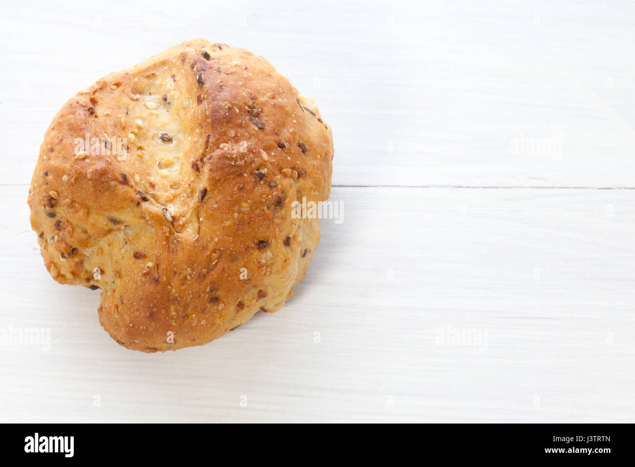 Single cereal bread bun on white wood table. Stock Photo