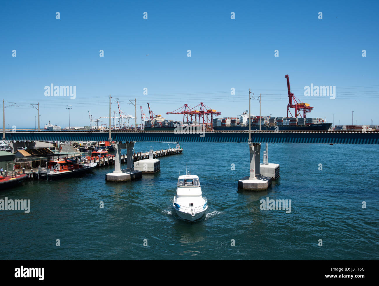 Yacht boating under railway bridge in the Swan River with commercial dock in Fremantle, Western