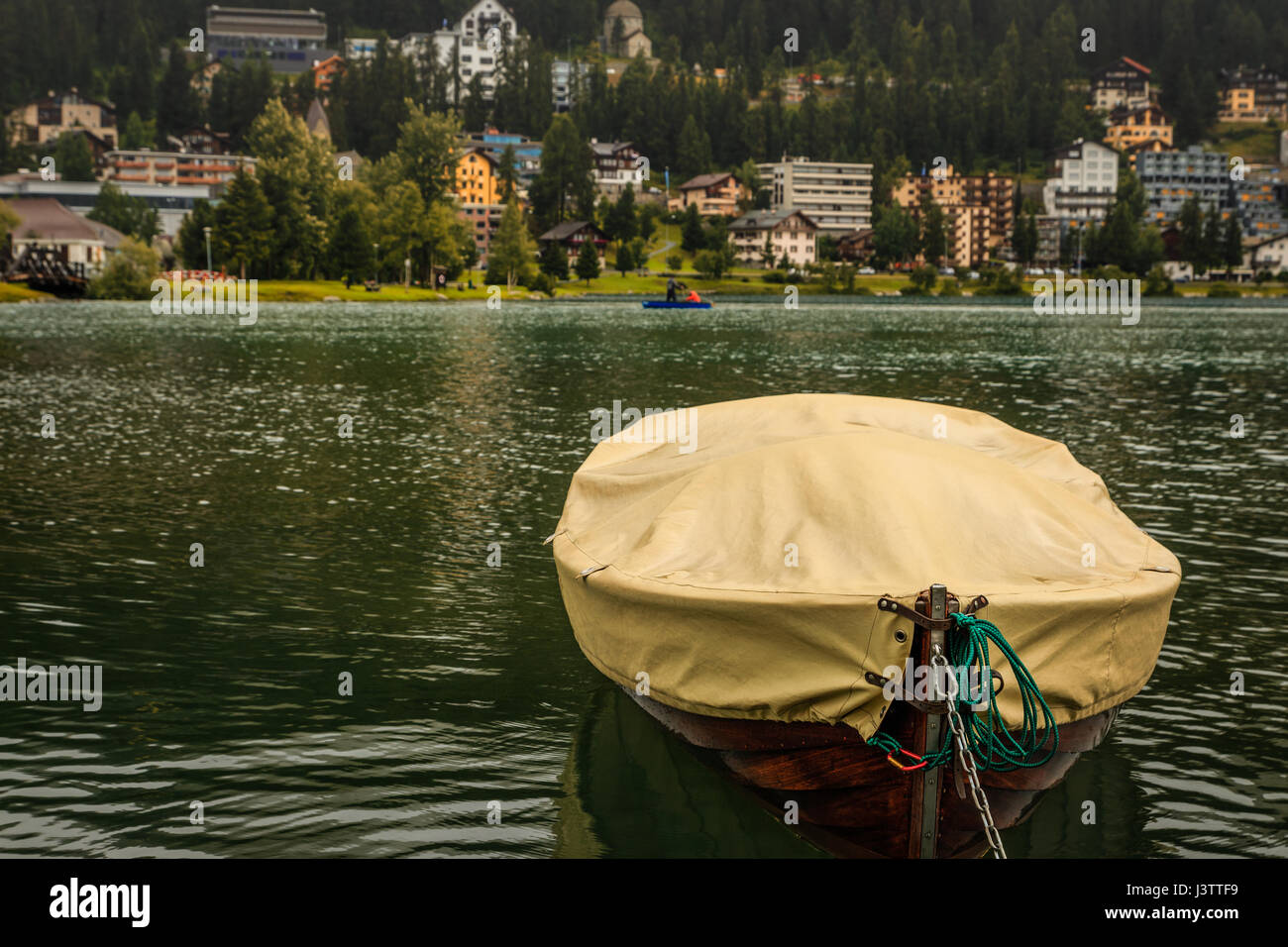 A small brown wooden boat under a yellow tarpaulin on the lake of St. Moritz. (Sankt Moritz, Engadin, Grisons, Switzerland) Stock Photo