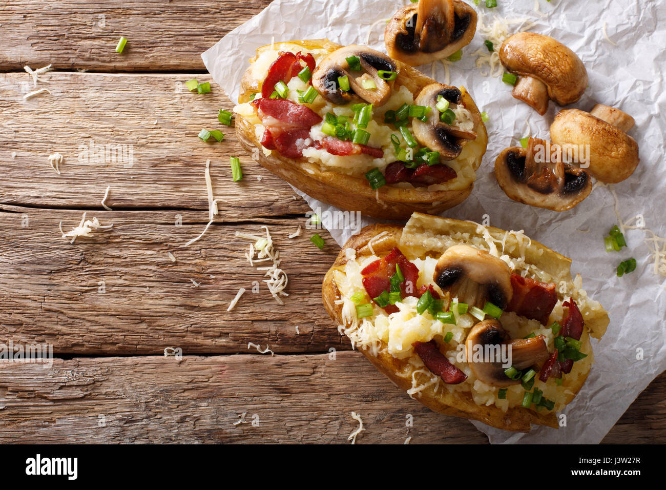 Hearty hot baked potatoes with bacon, mushrooms, onions and cheese close-up on the table. horizontal view from above Stock Photo