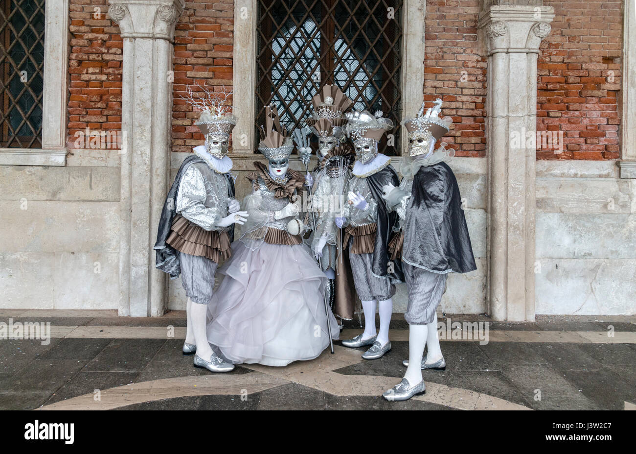 Image of five individuals in complementary ornate costumes along the Palace of the Doges during the Carnevale festival in Venice, Italy. Stock Photo