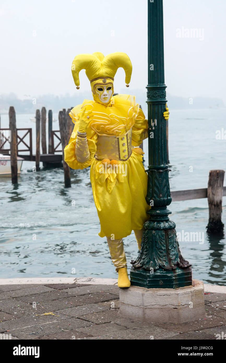 Image of an individual in a yellow colorful costume along the Grand Canal during the Carnevale festival in Venice, Italy. Stock Photo