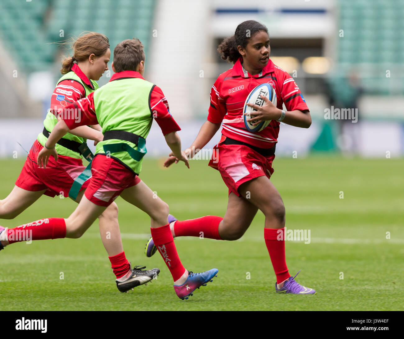 A girl runs with the ball in a mixed game of tag rugby for children involving girls and boys Stock Photo