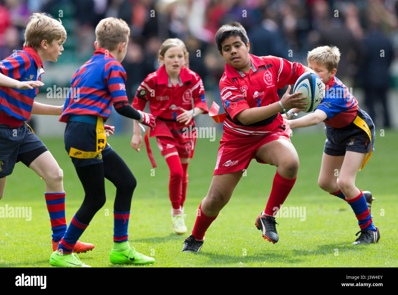 An Asian boy runs with the ball in a mixed game of tag rugby for children involving girls and boys Stock Photo